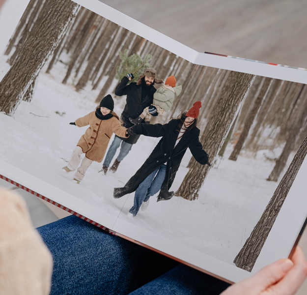 Women holding open a large photobook with a photo of a young book playing with a boogie board in the ocean