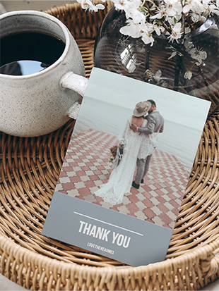 Card dispalyed in a wicker basket with a cup of coffe and flowers, the card has a couple on their wedding day with the text 'Thank You' underneath