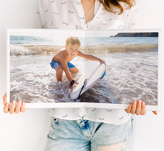 Women holding open a large photobook with a photo of a young book playing with a boogie board in the ocean