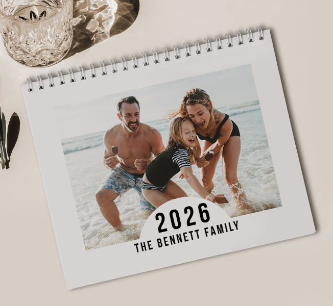 A calendar propped on a wooden table with a photo of two women hugging in the water with the text on the front 'Wanderlust Adventure Awaits, Go Find It'