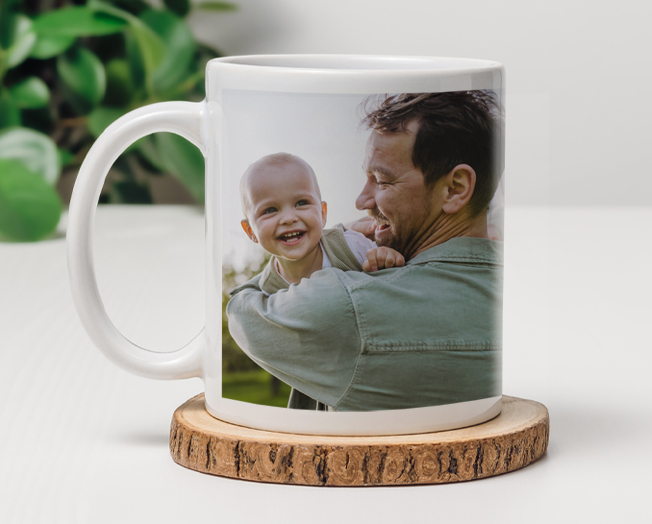 An orange cat drinks from a mug with an image of a mom and baby on the front with the text 'Love'