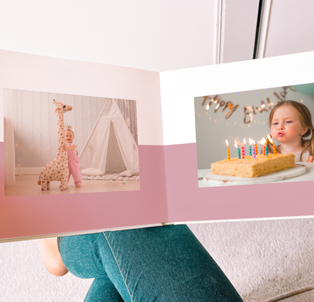 Women holding open a large photobook with a photo of a young book playing with a boogie board in the ocean