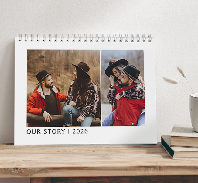 A calendar propped on a wooden table with a photo of two women hugging in the water with the text on the front 'Wanderlust Adventure Awaits, Go Find It'