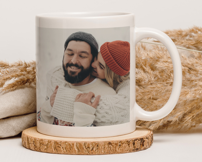 An orange cat drinks from a mug with an image of a mom and baby on the front with the text 'Love'